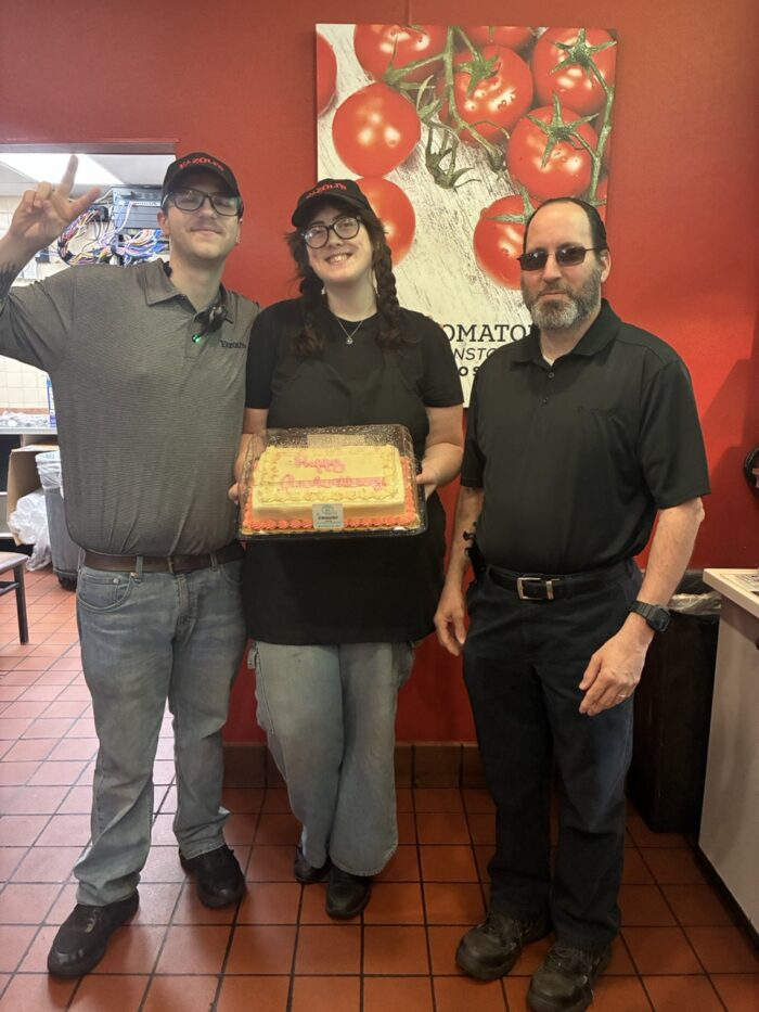 Associate Trainer Kiersten with two other employees holding a Happy Anniversary cake.