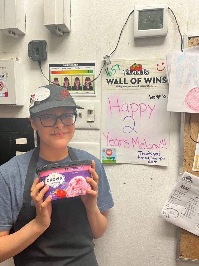 Melany standing with Strawberry Ice cream, in front of a sign stating Happy 2 Years Melany!!! Thank you for all that you do.