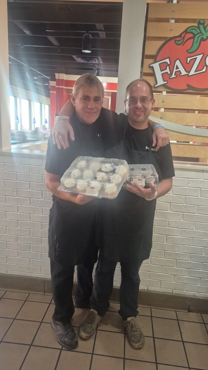 Associates Donald and Ben holding cupcakes in front of a Fazoli's sign.